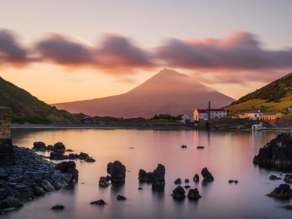 A view across the water of a peak in the Azores at sunset