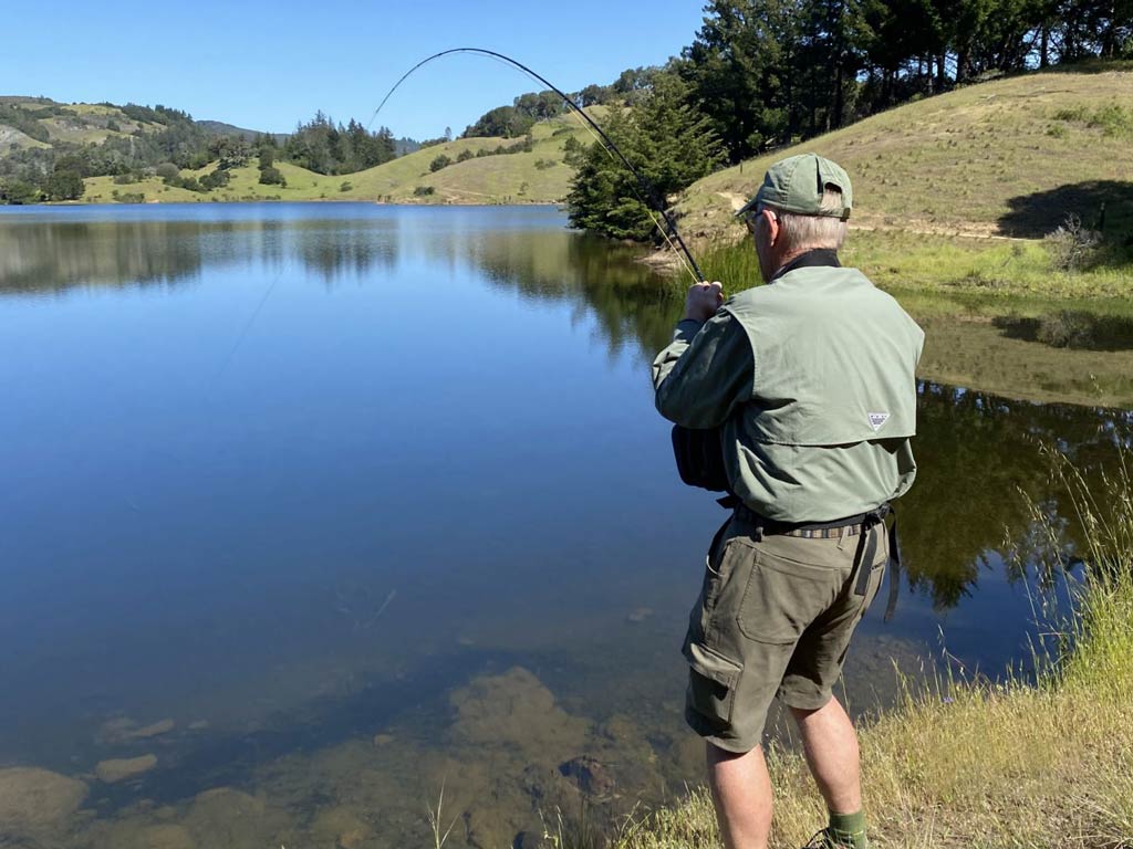 A rearview image of an angler standing on the shore and surf casting while trying to catch a California Delta fish during a sunny day