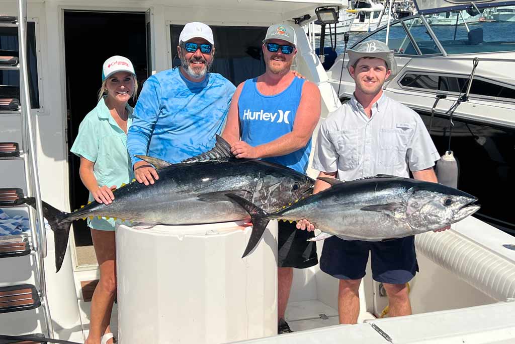 A group of four anglers standing on a boat with two Bluefin Tuna in front of them