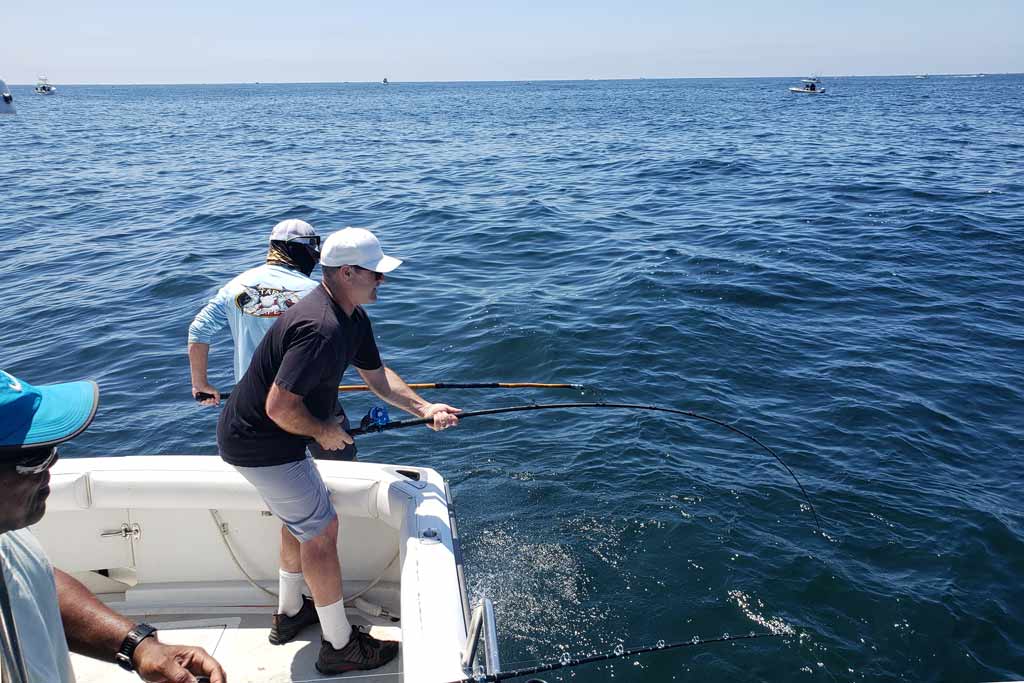 A fisherman holding onto a bent rod, with two more fishermen around him and with water in the background