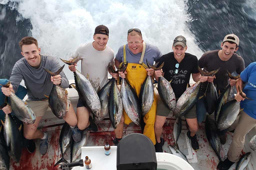 A group of anglers sitting on a boat rail, each holding two Bluefin Tuna