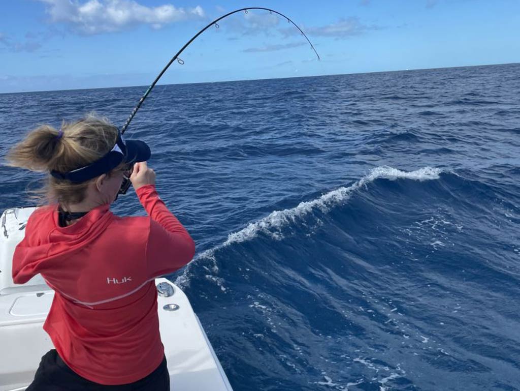 A female angler standing on a boat and bottom fishing on a cloudy day