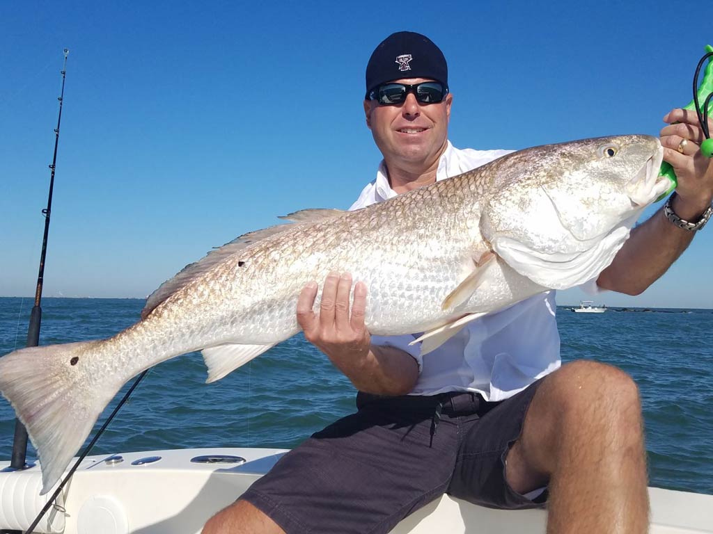 An angler sitting on a boat and holding a Bull Redfish with both hands