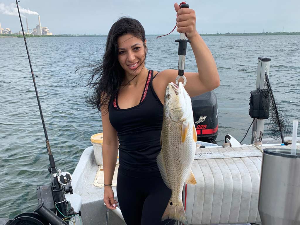 A woman on a boat, posing with a Redfish she caught fishing near Calaveras Lake power plant.