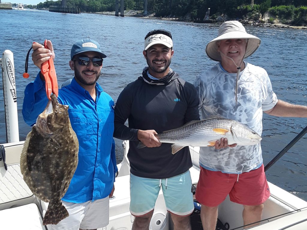 A group of three anglers standing on a fishing boat, smiling and holding freshly caught Flounder and Redfish, Carolina Beach, NC