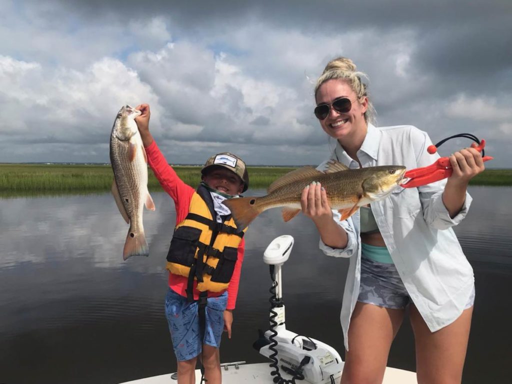 A female angler holding a freshly caught Redfish and a young angler holding a similar fish while standing on a fishing boat in Carolina Beach, NC