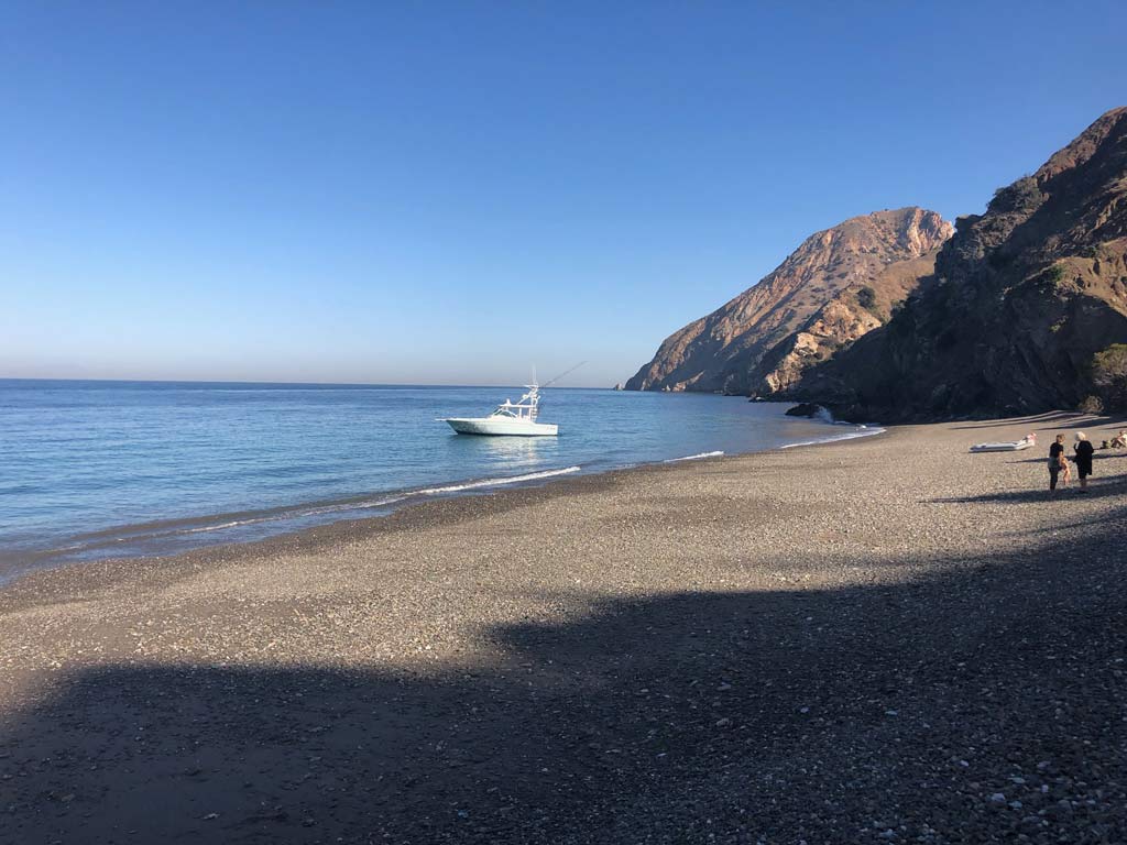 A charter boat parked next to a quiet beach on Catalina Island, while beachgoers lay on land.