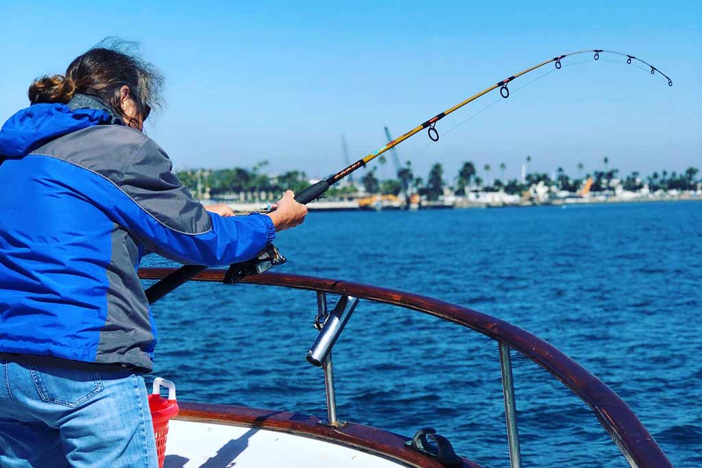 A man holding a bent fishing rod, fishing on a charter boat with San Diego in the background