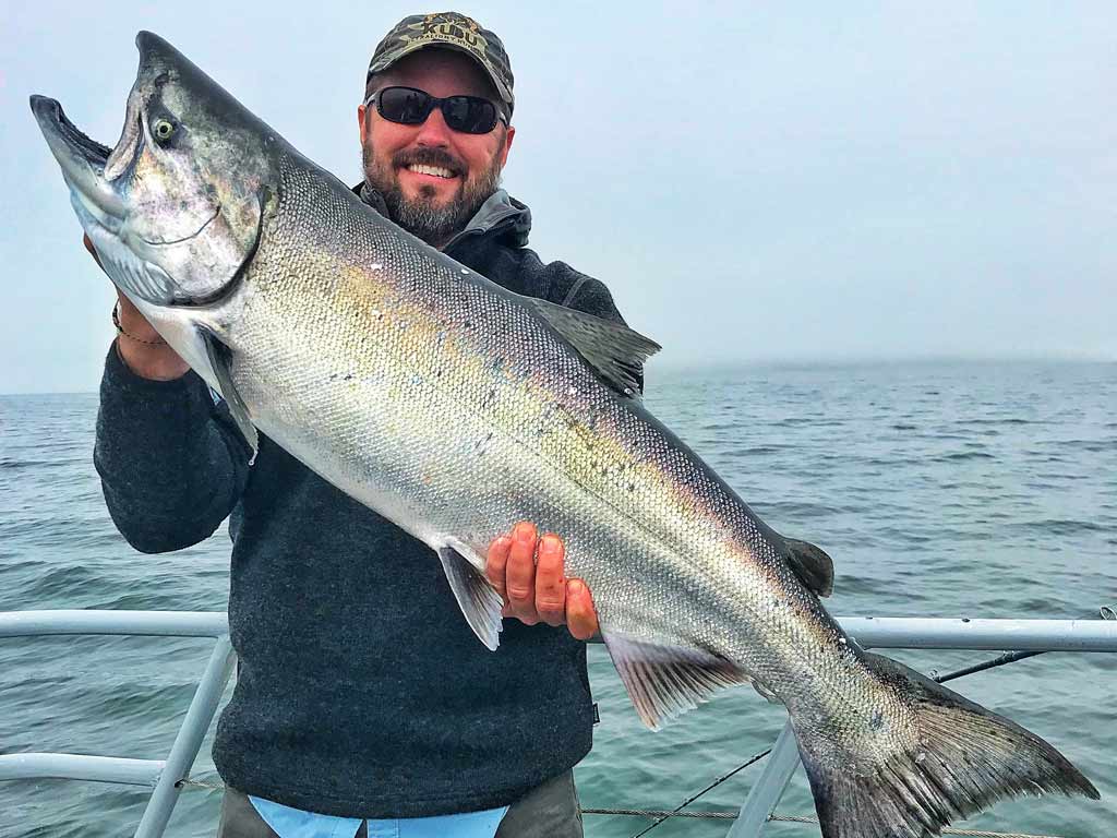 A smiling angler posing with a big Chinook Salmon he caught.