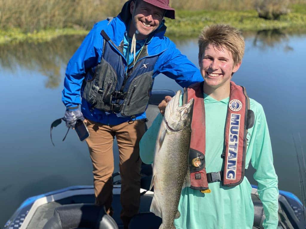 A photo of two happy anglers holding Salmon while standing on a boat located somewhere in the California Delta