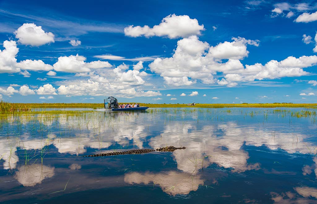A view across the water in the Everglades with a traditional Florida boat in the distance and reflections of the clouds on the water