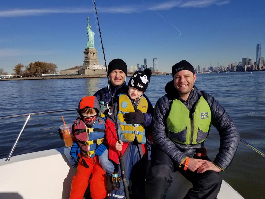 A lovely photo of a family with two kids sitting on a NYC charter fishing boat with an excellent view of the Statue of Liberty in the background