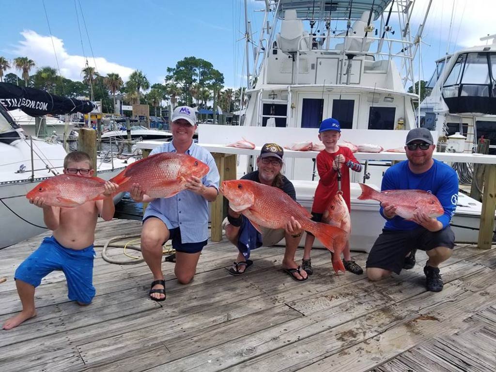 Група риболовци, след като са отишли ​​да ловят червени риби във Флорида, показват улова си на дока пред чартърна лодка
