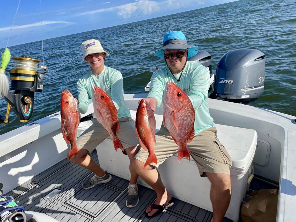 A father and his son sitting on an ice box on a charter boat and holding Red Snappers