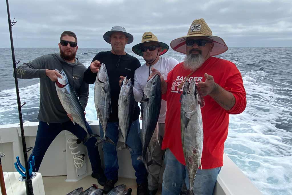 Four male anglers holding Bonito fish, standing on a fishing boat
