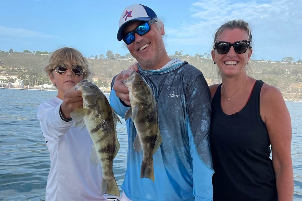 A smiling family on a boat, father and son holding Calico Bass