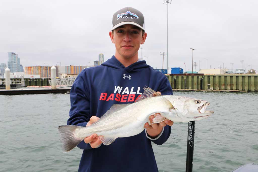 A young fisherman in a cap holding a Corvina fish on a dock in Mission Bay