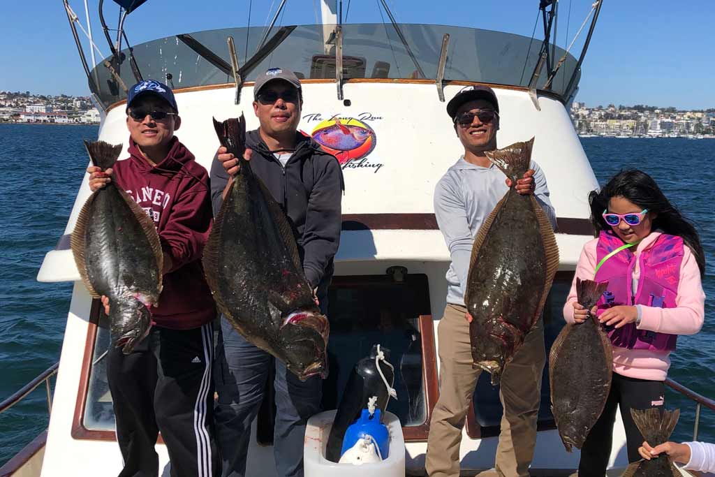 A group of anglers standing on a charter boat, each holding a Halibut