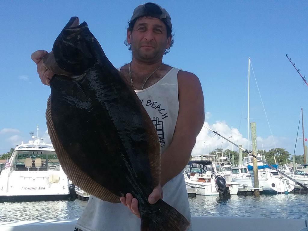 A photo of an angler standing in the marina on a docked charter fishing boat and showing off Flounder caught in New York City’s waters