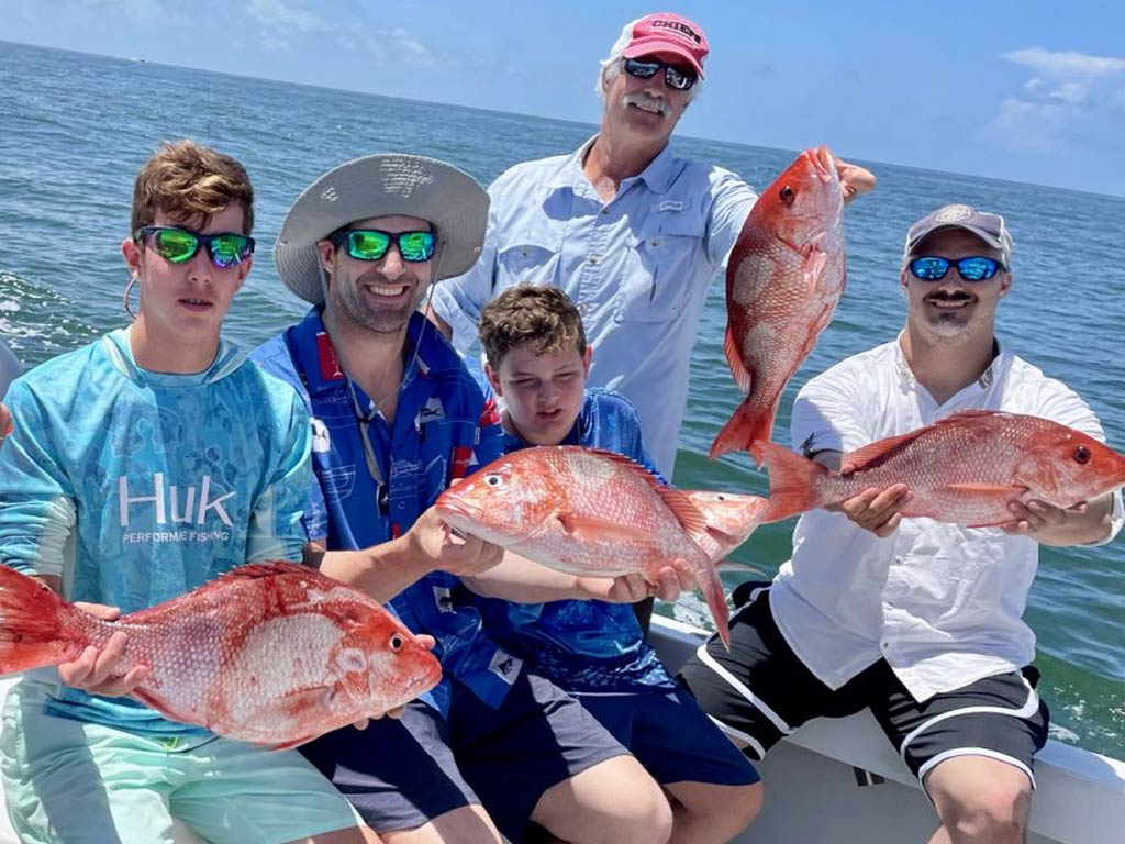 A group of anglers sitting on a charter boat and holding their Red Snapper catches