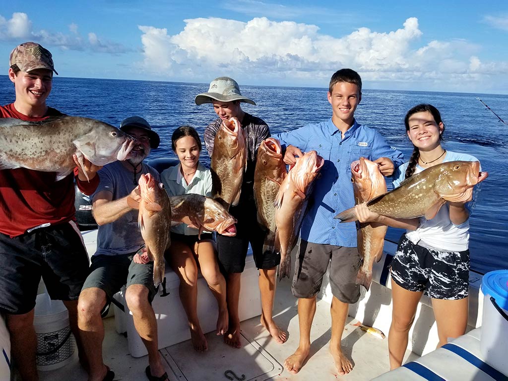 Група млади риболовци, които държат по един групер на кораб Cortez за дълбоководен риболов