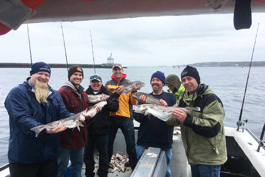 A group of fishermen standing on a charter boat, holding several Haddock fish they caught