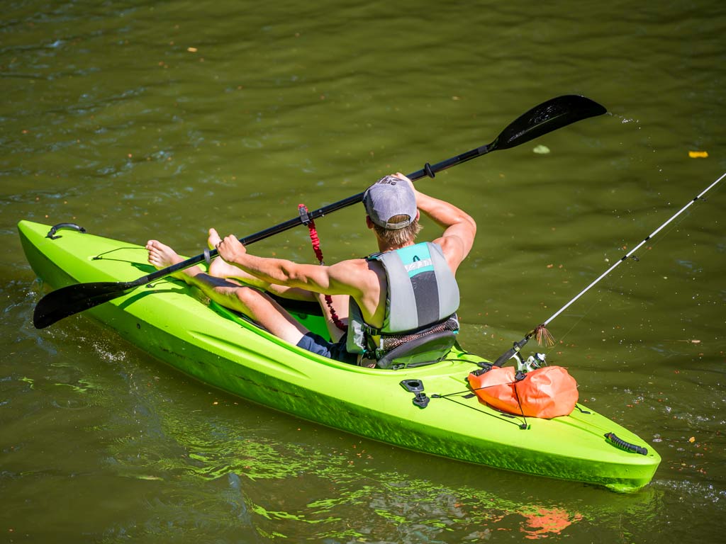 A kayak fisherman paddling through the waters, with his fishing rod behind him.