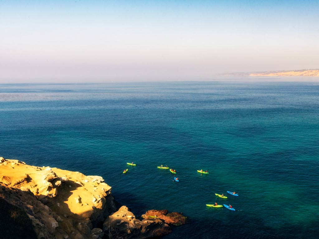 An aerial photo of kayakers gathered underneath La Jolla cliffs.