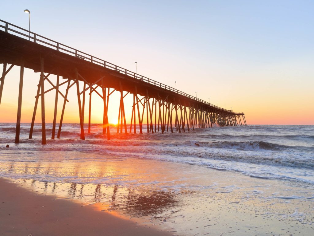 A view from the beach on Kure Beach Pier during the sunset on a clear day.