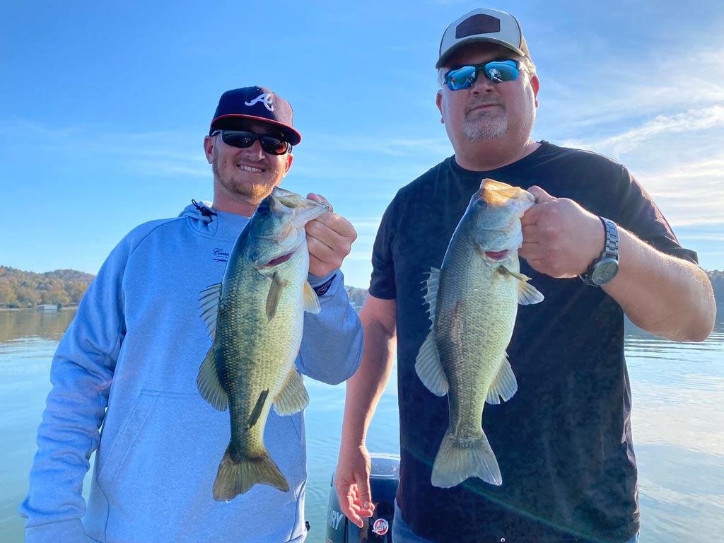 Two anglers posing for a photo, each holding a Largemouth Bass towards the camera.