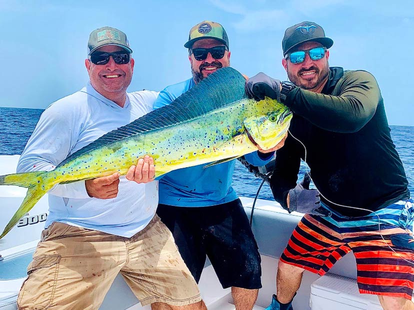 Three smiling male anglers standing on a fishing boat in Miami Beach, FL, and holding a Mahi Mahi