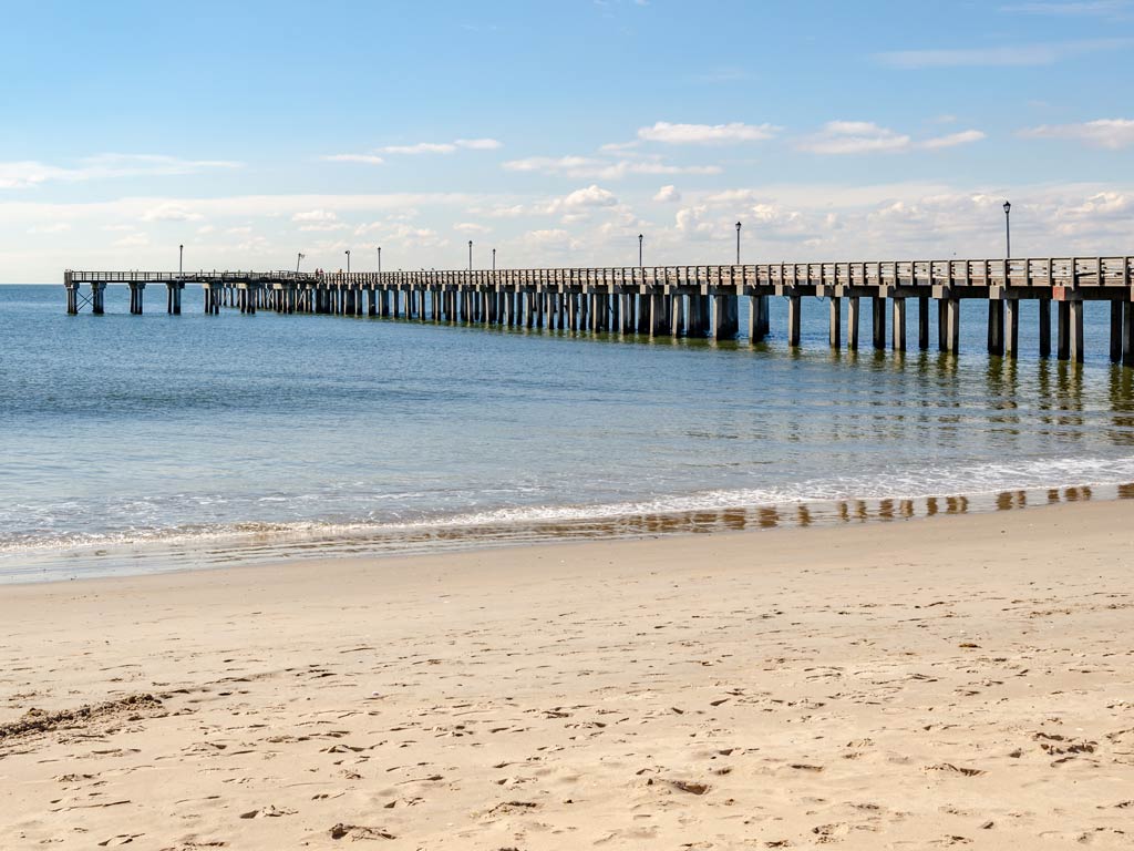 A side view of the sandy beach and famous Pat Auletta Steeplechase Fishing Pier in New York