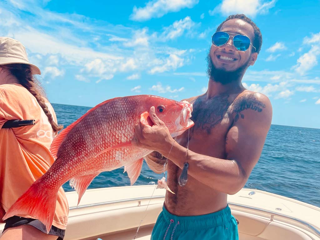 A smiling angler standing on a boat, posing with a Red Snapper he caught.