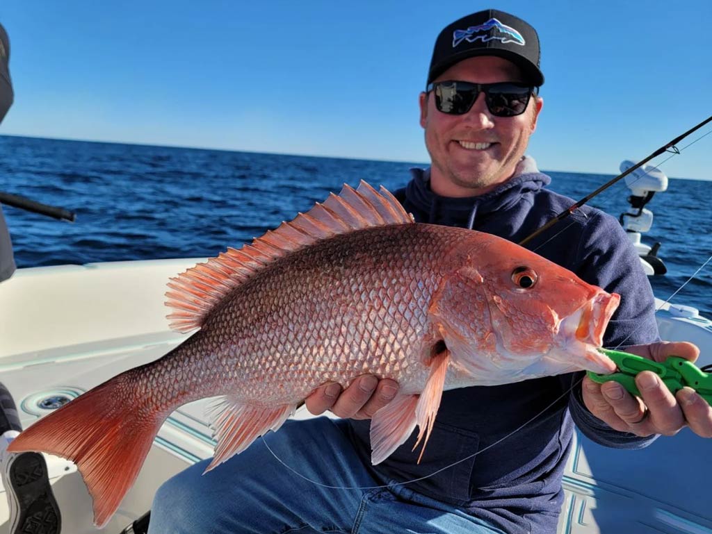 A photo of an angler siting on a boat and holding a big Red Snapper with both hands caught in the Gulf of Mexico