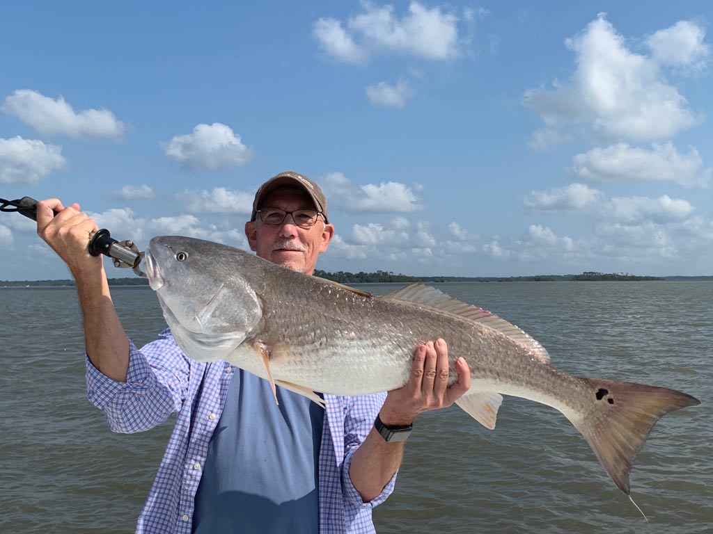 An elderly angler posing with a huge Redfish he caught inshore fishing in South Carolina.