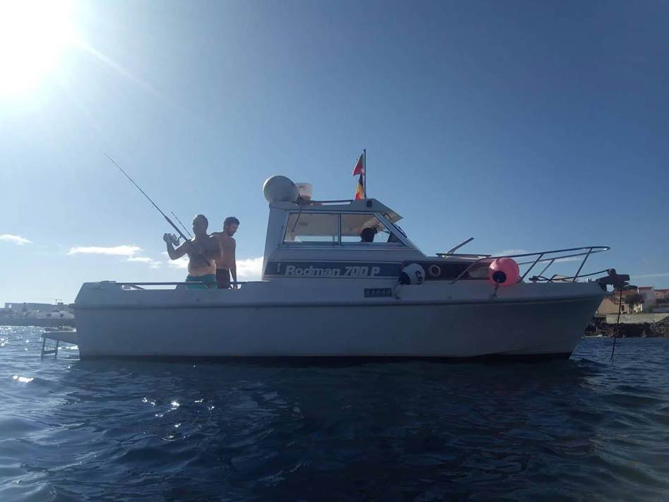 A view from the water of a boat nearshore in the Azores with people fishing from it on a sunny day