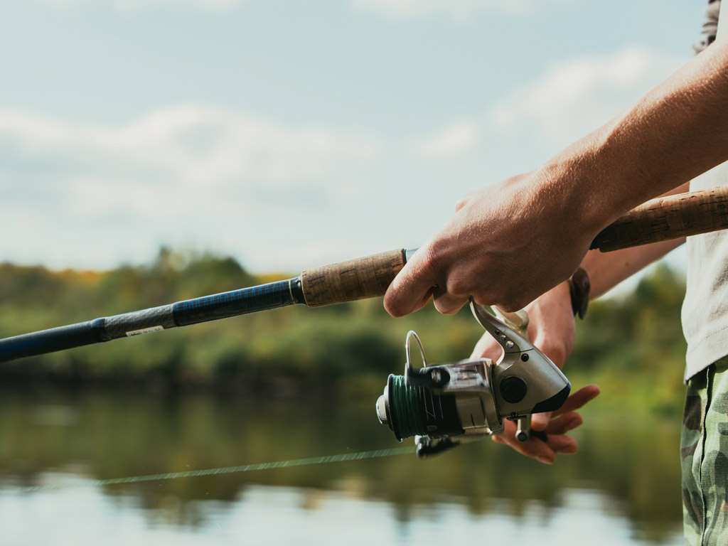 A closeup of photo of an angler's arms holding a rod and reeling in the line.