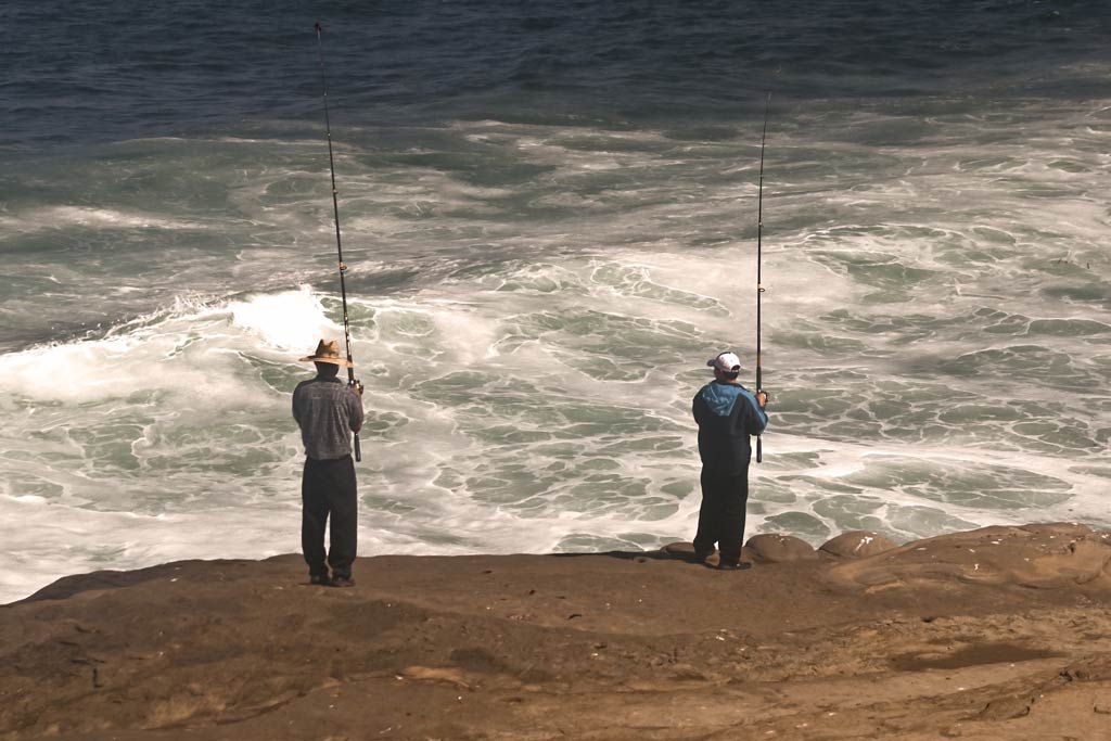 Two shore fishermen standing on a jetty, casting into the surf below them