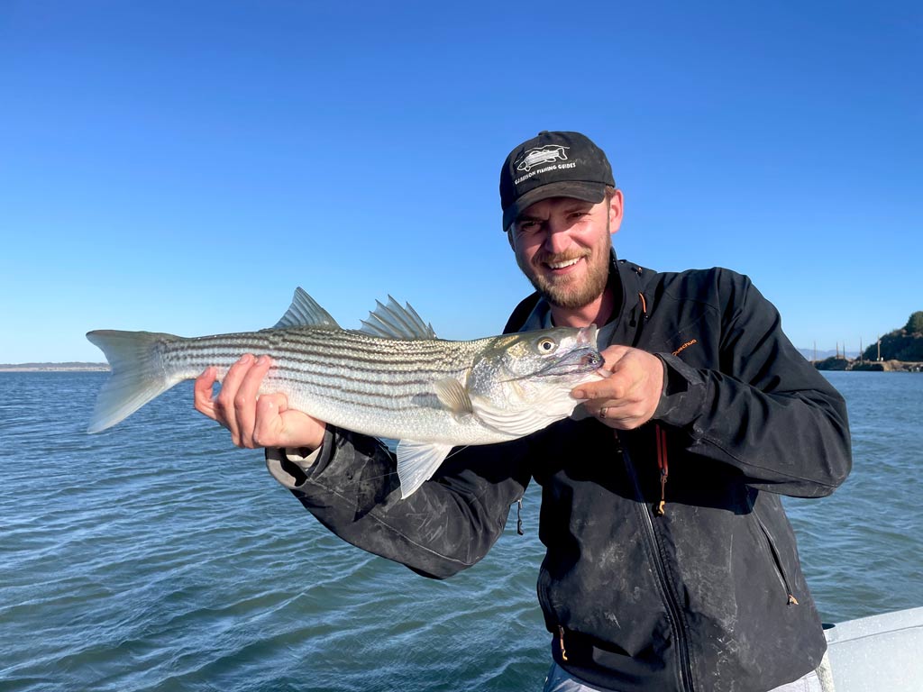 A smiling angler posing with a Striped Bass he reeled in in San Francisco Bay.