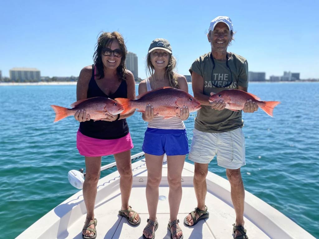 Three anglers standing on a Florida fishing charter and holding Red Snapper each with a built-up city behind them