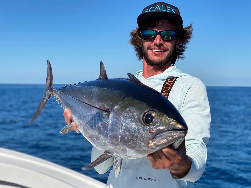 A smiling angler in a cap and sunglasses holding a large Tuna caught in Cortez