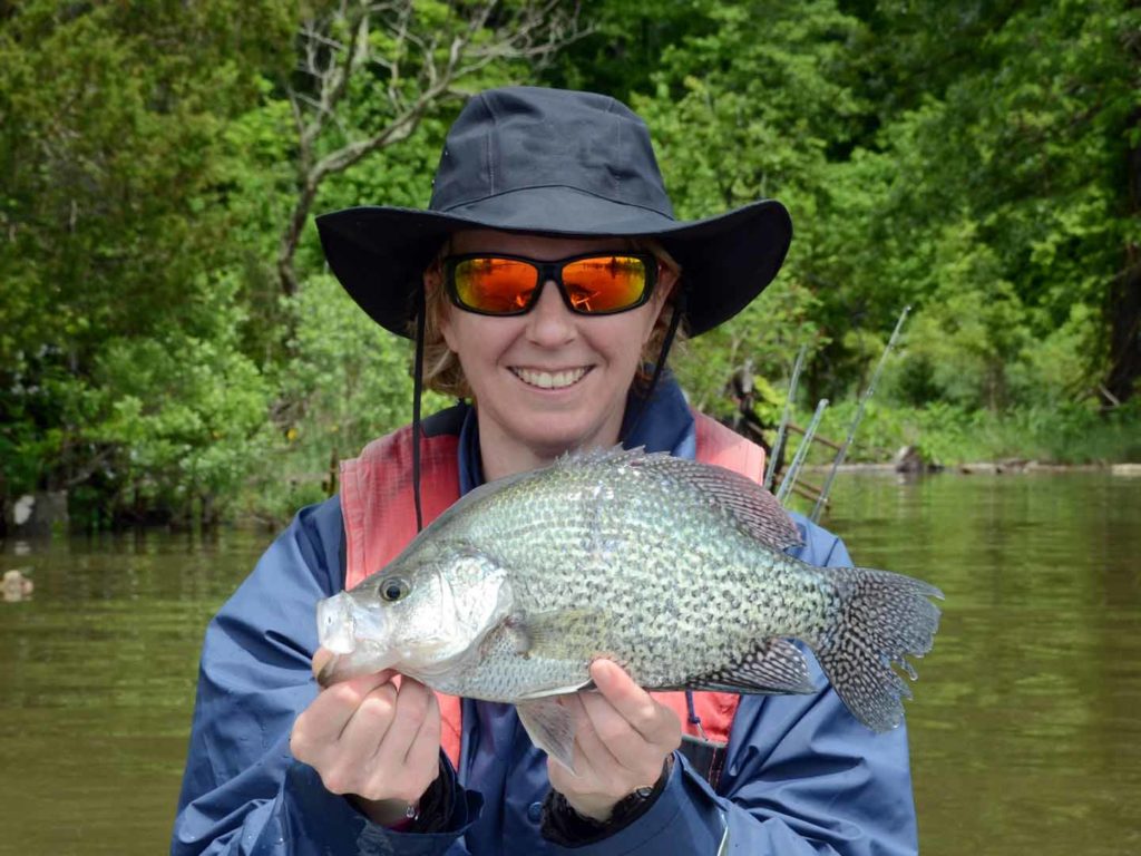 A woman holding a Crappie on a boat on a lake