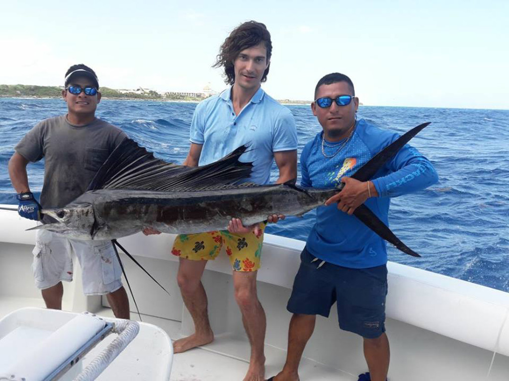 Three anglers on a boat holding a Sailfish they caught on a deep sea trip in Cozumel.