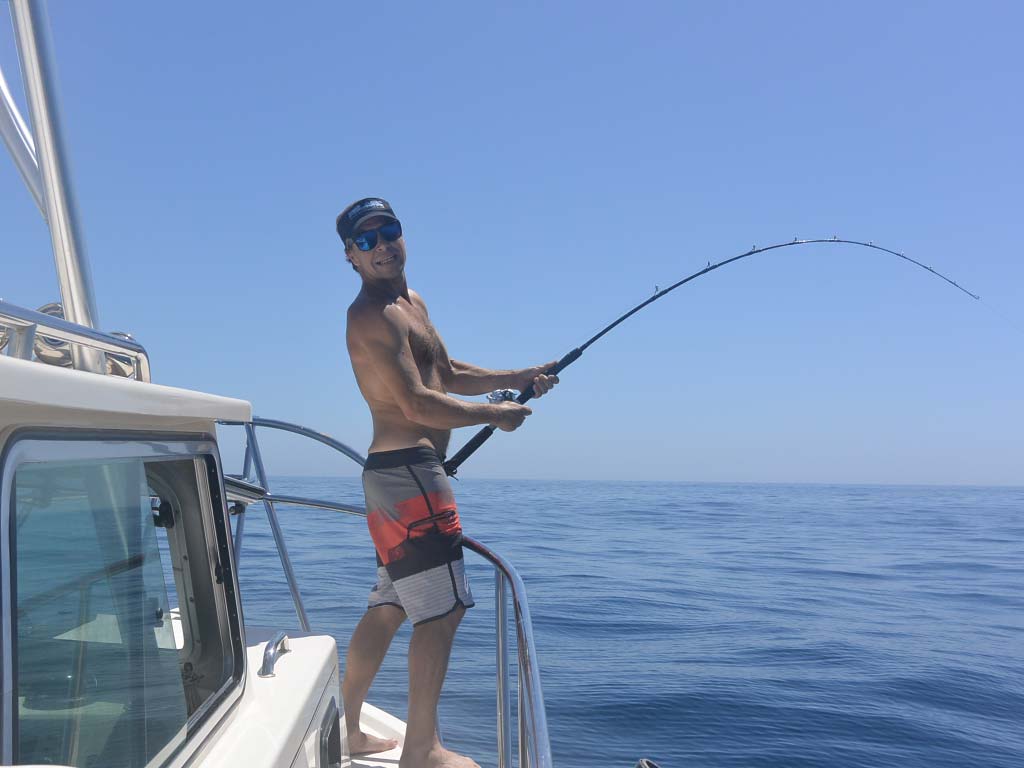 An angler stands on the side of a boat holding a fishing rod.