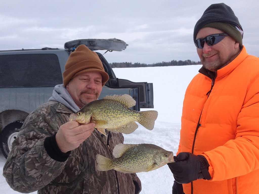 Two anglers comparing the sizes of the fish they caught during their ice fishing trip in Wisconsin.