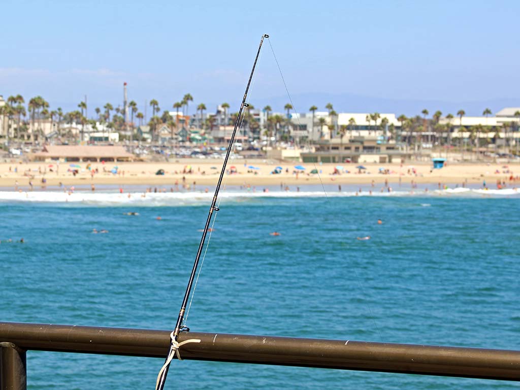 A lone fishing rod on a pier overlooking Huntington Beach.