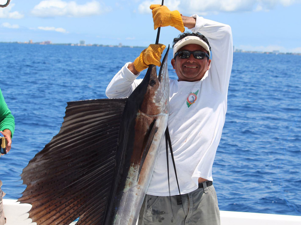 A smiling angler holds up a Sailfish he recently caught on a deep sea trip in Cozumel.