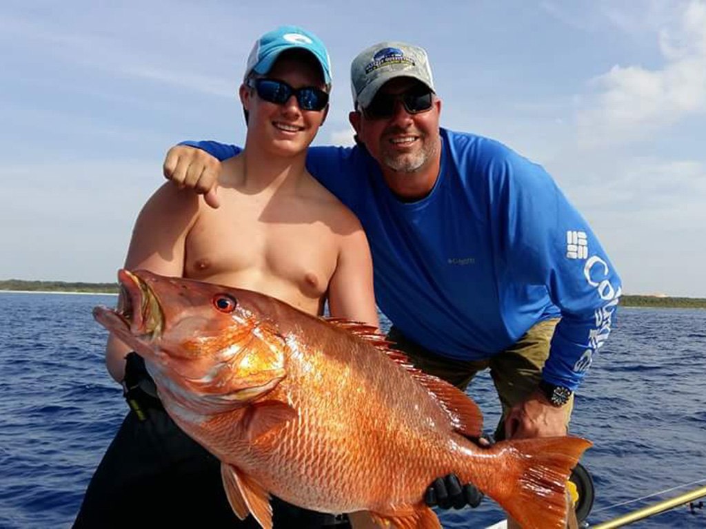 A pair of happy anglers holding a Cubera Snapper they just caught on a deep sea fishing trip in Cozumel.