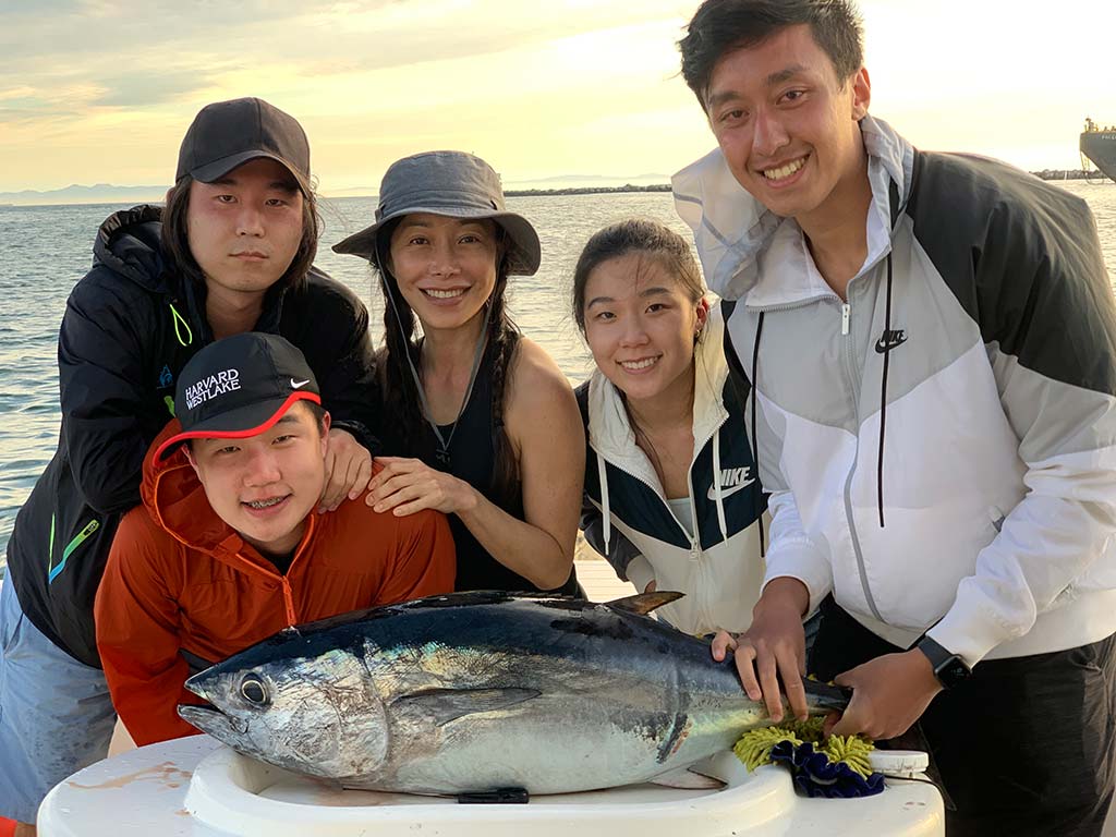 A happy family take a photo next to a Tuna they caught during a fishing trip.