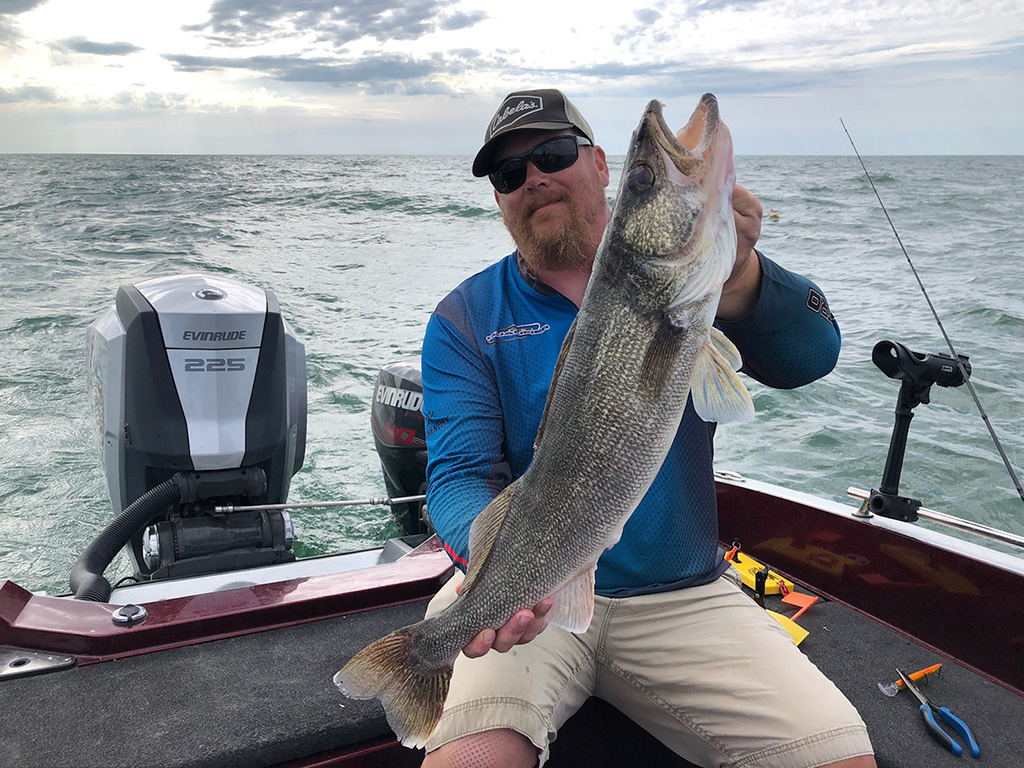 An angler sitting on the back of a boat holds up a Walleye he caught on a Wisconsin fishing trip.